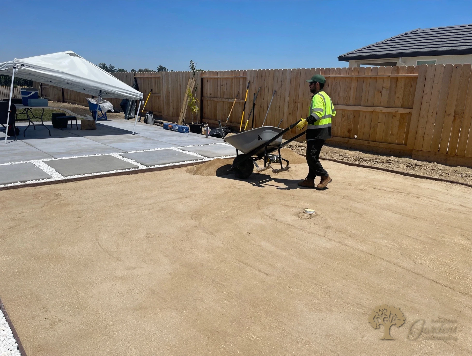 American Gardens Landscaping crew member spreading decomposed granite with a wheelbarrow beside concrete pavers during a DG installation