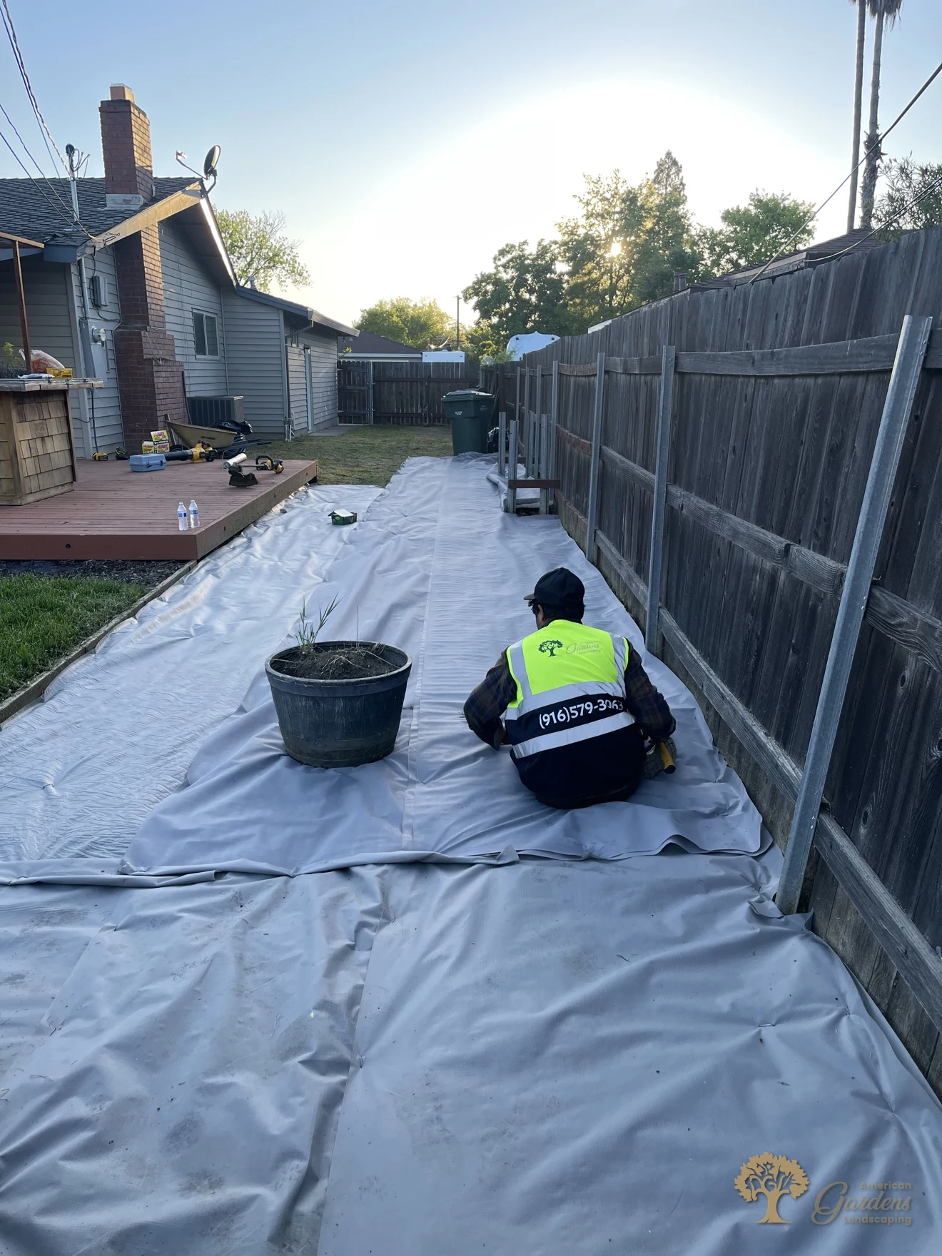 Crew member securing weed fabric along a fence during a xeriscape conversion in Carmichael