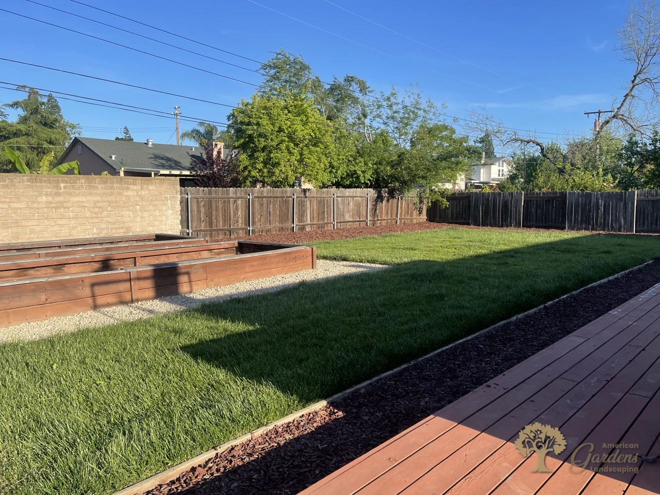 Finished backyard xeriscape in Carmichael with gravel around raised beds, a bark band and clean lawn